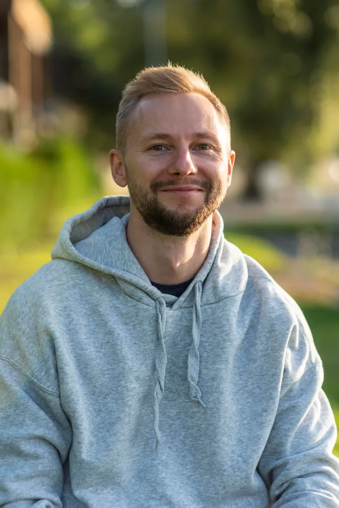 A man wearing a grey hoodie and smiling.